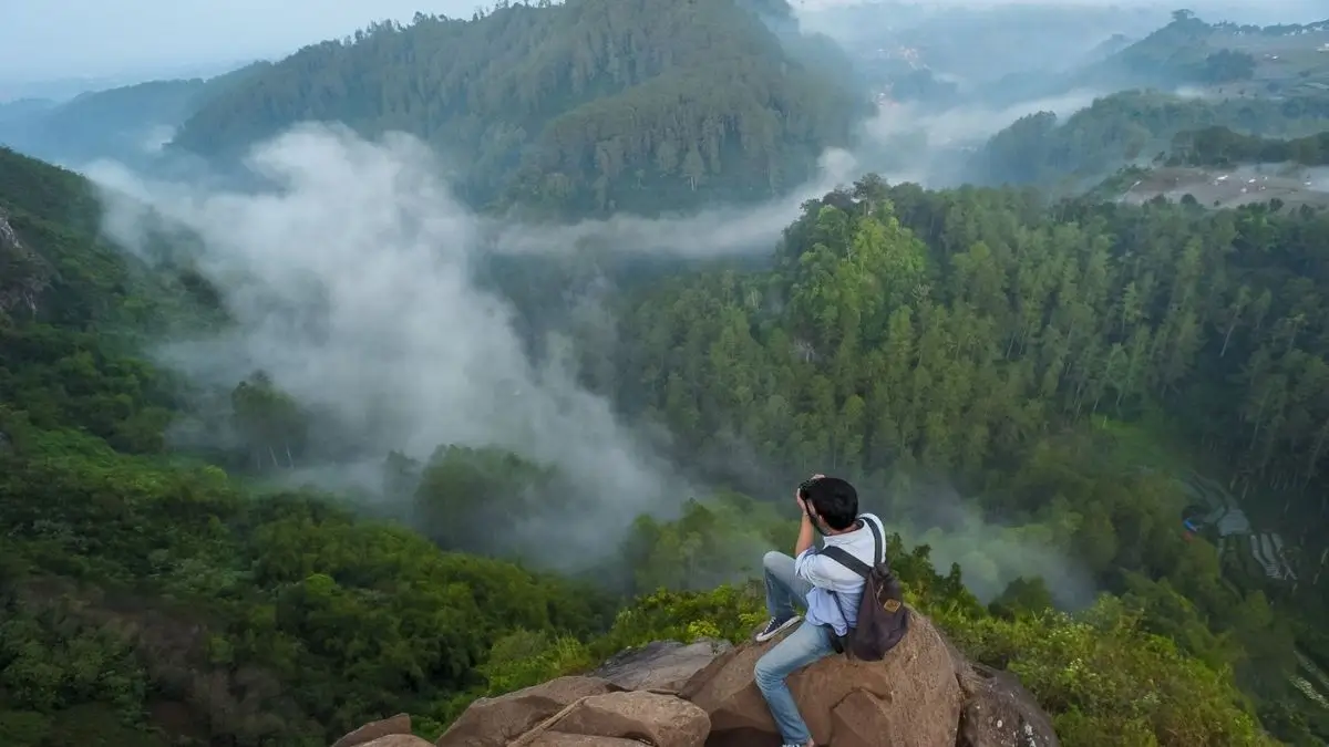 seorang pria duduk diatas batu di tempat wisata tebing keraton dago bandung